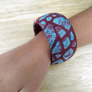 Könnte beinhalten: Ein breites, braunes Stoffarmband mit einem blauen und braunen geometrischen Muster.