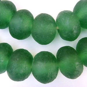 May include: A close-up of a strand of green glass beads. The beads are oval-shaped with a textured surface and a translucent appearance. The beads are a deep, rich green colour, and are strung together.