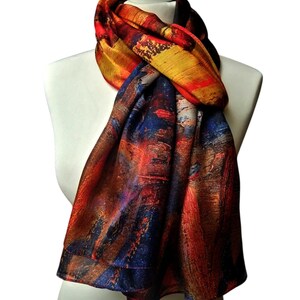 Peut inclure: Écharpe colorée avec un motif abstrait. Elle présente un mélange de rouge, d'orange, de jaune et de bleu. L'écharpe est drapée sur un mannequin blanc, mettant en valeur son tissu fluide et son motif artistique.