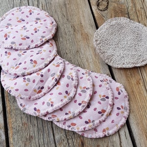 Op de afbeelding: Een set van acht herbruikbare make-up remover pads met een roze achtergrond en een patroon van kleine, kleurrijke bladeren. De pads zijn gemaakt van zacht materiaal en hebben een gestikte rand.