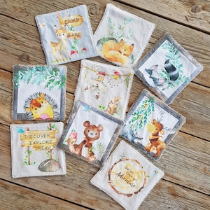 Könnte beinhalten: Neun quadratische Stoffstücke mit verschiedenen Waldtierillustrationen und Text. Die Patches zeigen ein Reh, einen Fuchs, einen Waschbär, einen Igel, einen Bären, einen Elch und einen Baumstumpf mit dem Text "Wähle immer Abenteuer".