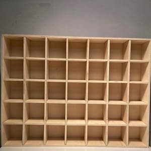 Puede incluir: Una estantería de madera con 36 compartimentos individuales. La estantería está hecha de madera clara y tiene un diseño simple y minimalista.