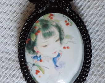 Grande broche ovale ,noire,cabochon en verre,motif jeune fille,coloris brun,bleu,rouge ,fond blanc.