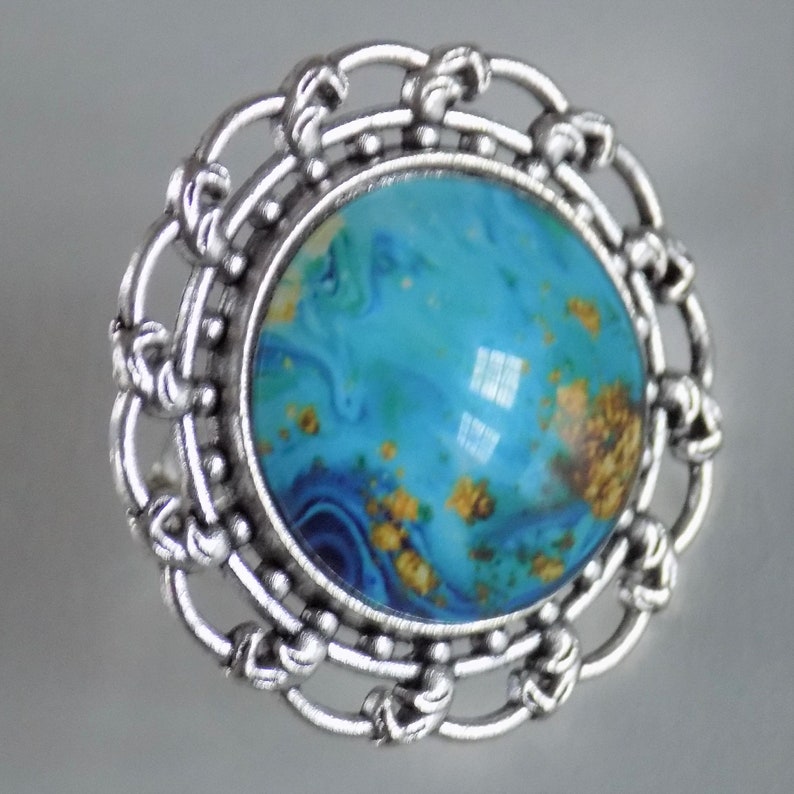 May include: A silver ring with a blue and gold marbled cabochon stone set in a decorative filigree design.