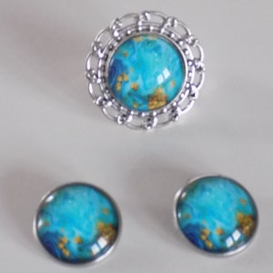 May include: A silver ring with a blue and gold swirl design, and a pair of matching earrings.