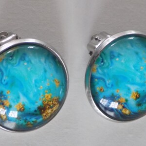 May include: A pair of silver clip-on earrings with a round blue, white, and gold abstract design.