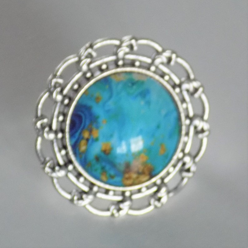 May include: A silver ring with a blue and gold agate stone set in a decorative filigree design.