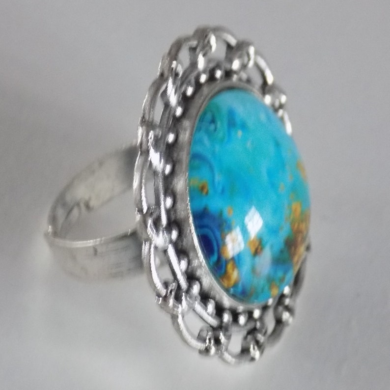 May include: A silver ring with a blue and gold swirl design in the center. The ring has a decorative filigree design around the center stone.