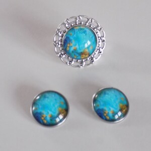 May include: A set of jewelry featuring a ring and earrings. The ring has a silver filigree design and a blue and gold cabochon. The earrings are silver with blue and gold cabochons.