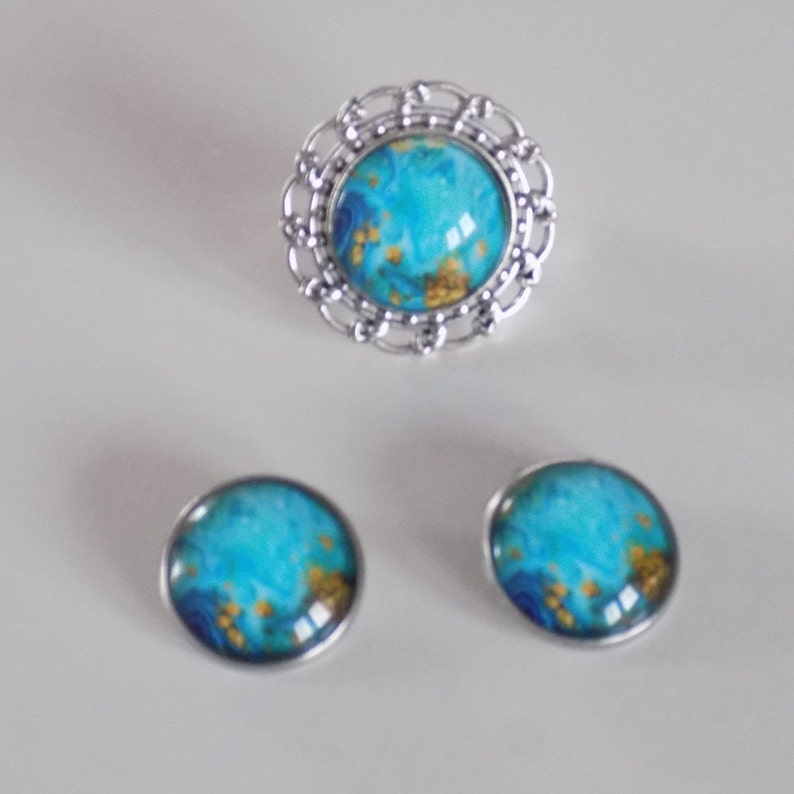 May include: A set of jewelry featuring a ring and earrings. The ring has a silver filigree design and a blue and gold cabochon. The earrings are silver with blue and gold cabochons.