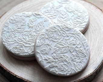 May include: Three white round cookies decorated with a raised white floral design. The cookies are on a wooden surface.