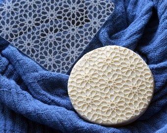 May include: Two white silicone cake decorating stencils with a geometric pattern. The stencils are on a blue fabric background.
