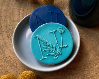 May include: Two blue and turquoise cookie cutters with floral designs. The cutters are shaped like the letter N and a flower.