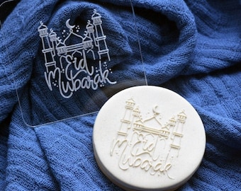 May include: A clear acrylic stamp with a white design of a mosque and the text "Eid Mubarak". A white silicone stamp with the same design is also shown.