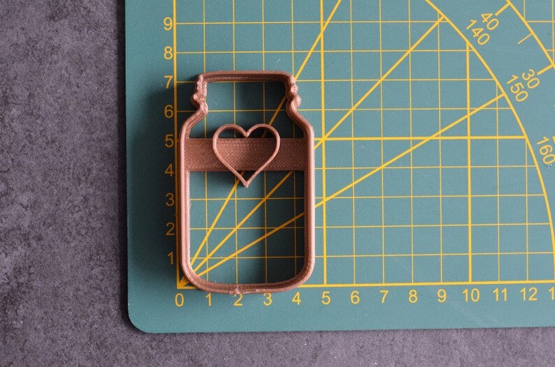 May include: A brown metal cookie cutter shaped like a mason jar with a heart cutout in the center.