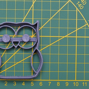 May include: A gray plastic owl cookie cutter on a green cutting mat with white grid lines.
