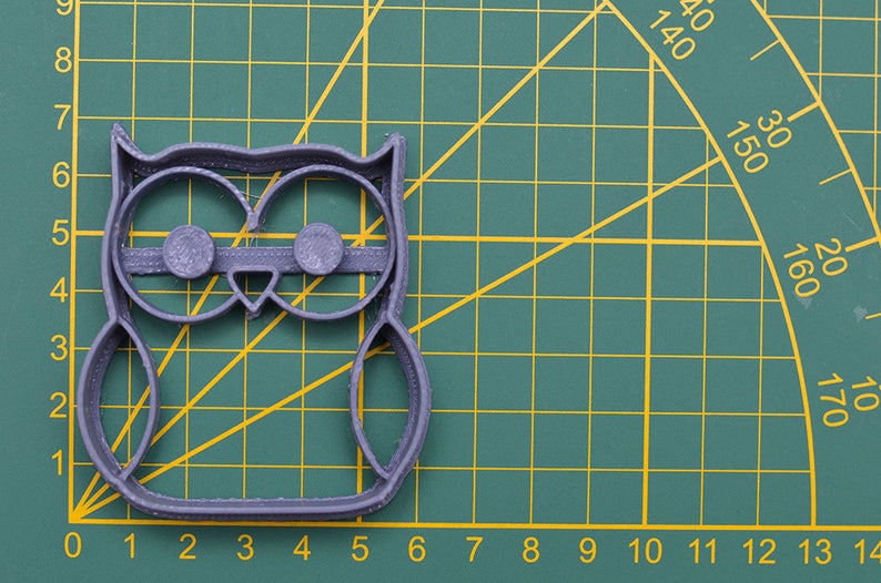May include: A gray plastic owl cookie cutter on a green cutting mat with white grid lines.