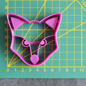 K&ouml;nnte beinhalten: Ein rosa Plastik-Keksstempel in Form eines Fuchses auf einer gr&uuml;nen Schneidematte.
