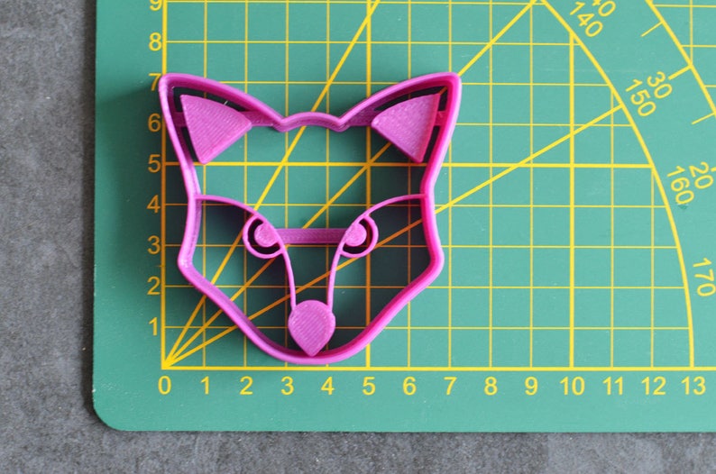 K&ouml;nnte beinhalten: Ein rosa Plastik-Keksstempel in Form eines Fuchses auf einer gr&uuml;nen Schneidematte.