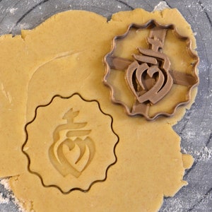 May include: A brown cookie cutter with a decorative design is pressed into a round piece of cookie dough.