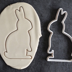 May include: A white cookie cutter in the shape of a rabbit, with a white fondant cookie dough cutout in the shape of a rabbit.