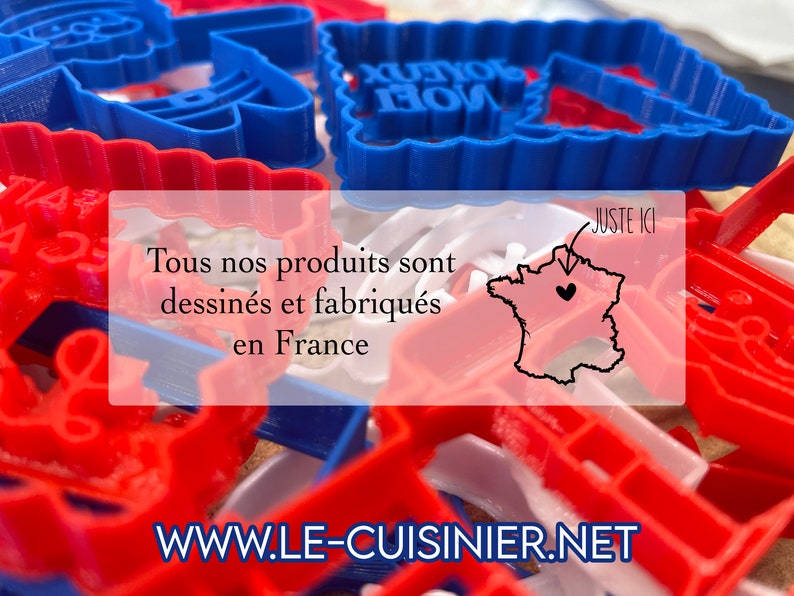 May include: A close-up of red and blue plastic cookie cutters in various shapes, including a Christmas tree, a bell, and the words "Joyeux Noel". The text "Tous nos produits sont dessin&eacute;s et fabriqu&eacute;s en France" and "www.le-cuisinier.net" are also visible. A map of France with a heart in the center is labeled "Juste Ici".