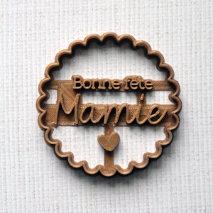 May include: Brown plastic cookie cutter with a scalloped edge. The cutter features the text "Bonne fete Mamie" and a small heart.