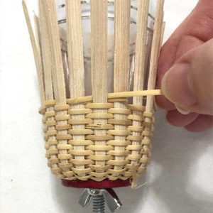 May include: A woven wicker basket with a red base and a metal screw clamp. The basket is being held in place by a rubber band.