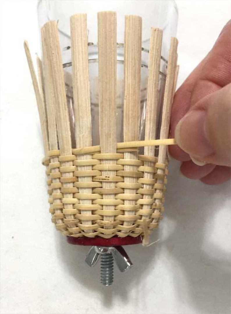 May include: A woven wicker basket with a red base and a metal screw clamp. The basket is being held in place by a rubber band.