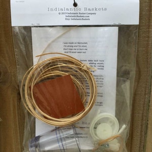 May include: A kit for making a small basket, containing a roll of natural reed, a small piece of brown leather, a clear plastic container, a white plastic ring, a rubber band, and a small metal hook. The kit comes with instructions and a poem about the history of Nantucket baskets.