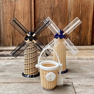 May include: Three miniature wicker windmills, one with black blades, one with white blades, and one with a blue top and white blades. A small wicker basket with a white handle and a white shovel is in the foreground.