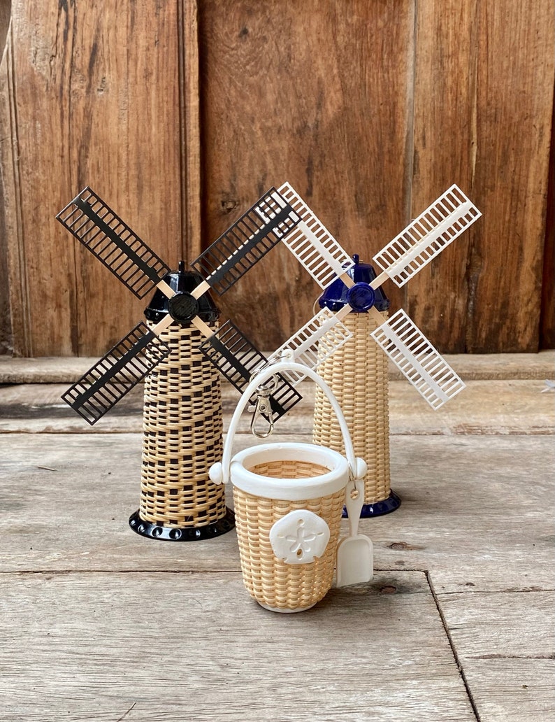 May include: Three miniature wicker windmills, one with black blades, one with white blades, and one with a blue top and white blades. A small wicker basket with a white handle and a white shovel is in the foreground.