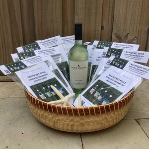 May include: A wicker basket filled with multiple packages of Nantucket Style Sand Pail Ornament Kits. The kits include instructions and all the materials needed to create a sand pail ornament. A bottle of white wine is also included in the basket.
