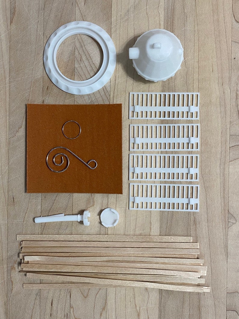 May include: A kit for building a model of a lighthouse. The kit includes white plastic pieces, wooden dowels, a brown felt sheet, and a metal wire.