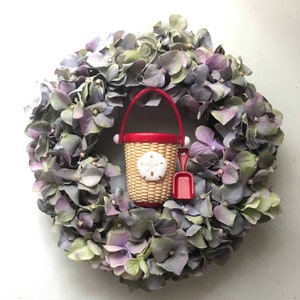 May include: A purple and green floral wreath with a red and white plastic bucket and shovel in the center. The bucket has a seashell design.
