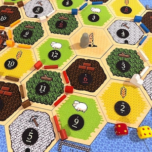 May include: A board game with hexagonal tiles depicting various resources like wood, brick, and wheat. Wooden pieces, dice, and number tokens are scattered across the board. The game board is blue and beige with a variety of colors.