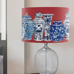 May include: A table lamp with a red lampshade featuring a pattern of blue and white porcelain vases. The lamp base is a clear, wire mesh design.