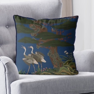 May include: A blue throw pillow with a dark blue border features a stylized illustration of two cranes standing in a forest with a large tree. The background is a deep blue color.