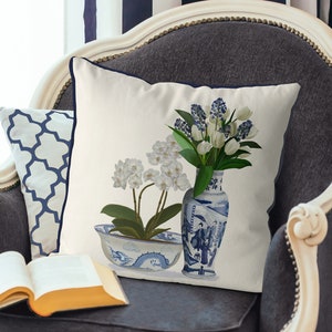 May include: A white pillow with a blue and white floral design. The pillow features a blue and white porcelain vase with a floral design and a blue and white porcelain bowl with a dragon design. The pillow is sitting on a gray chair.