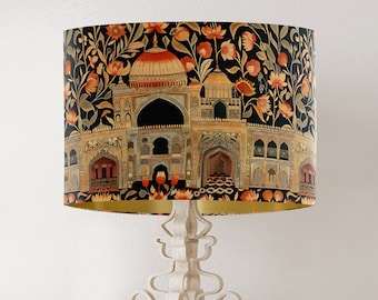 May include: A black and gold lampshade with a floral pattern and an intricate design of an Indian palace. The lampshade is on a white metal lamp base.