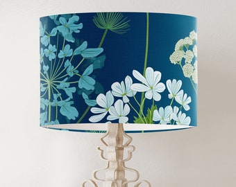May include: A white lamp with a blue and green floral patterned lampshade. The lampshade features white flowers and green leaves on a dark blue background.
