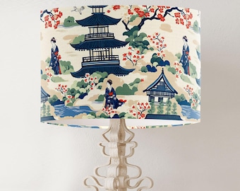May include: A white lampshade with a Japanese-inspired design featuring a pagoda, cherry blossoms, and figures in traditional clothing. The lampshade is on a white lamp base with a decorative design.