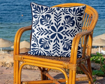 May include: A blue and white patterned throw pillow with a floral design sits on a wicker chair. The chair is on a patio with a view of the ocean.