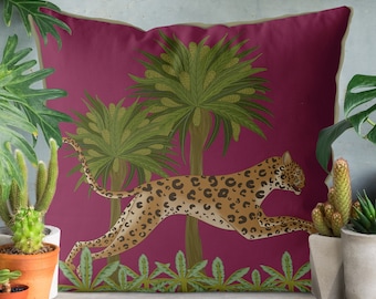Op de afbeelding: Een roze kussen met een luipaardprint die door een jungle scène met palmbomen loopt. Het kussen heeft een beige rand.