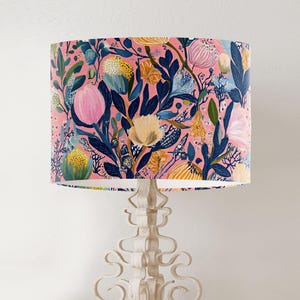 May include: A pink lampshade with a floral pattern featuring blue, yellow, and green flowers. The lampshade is made of fabric and has a white trim.