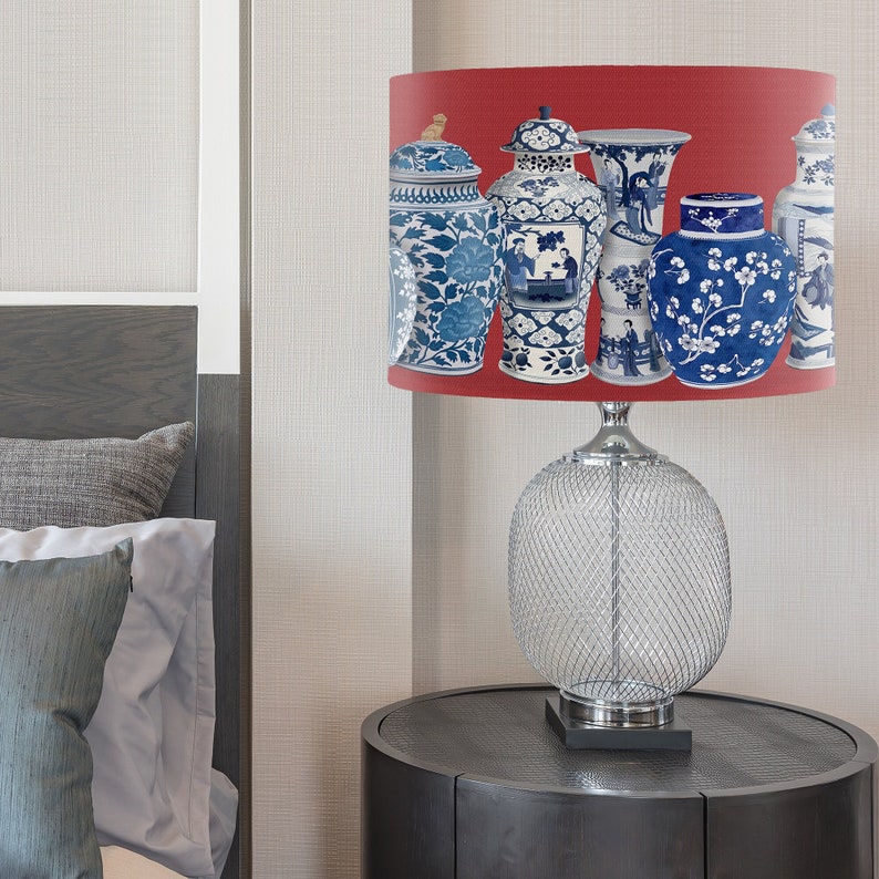 May include: A table lamp with a red lampshade featuring a pattern of blue and white porcelain vases. The lamp base is a clear, wire mesh design.