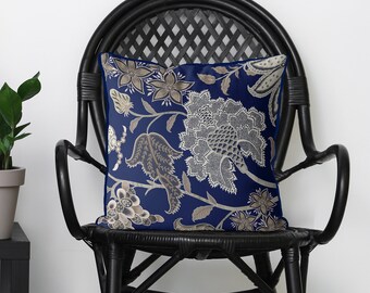 May include: A navy blue throw pillow with a white and gold floral pattern. The pillow is sitting on a black wicker chair.