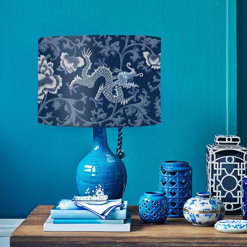 May include: A blue ceramic table lamp with a blue and white dragon patterned lampshade. The lamp is on a wooden table with other blue and white ceramic decorative items.