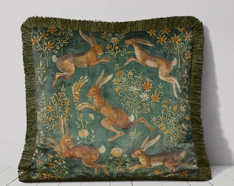 May include: A green velvet throw pillow with a fringe border features a repeating pattern of brown rabbits hopping through a field of yellow and orange flowers.