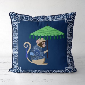 Könnte beinhalten: Ein blaues Kissen mit weißem Rand zeigt einen Affen, der ein blau-weiß gemustertes Hemd trägt und einen grünen Regenschirm mit Quasten hält. Der Hintergrund ist dunkelblau.